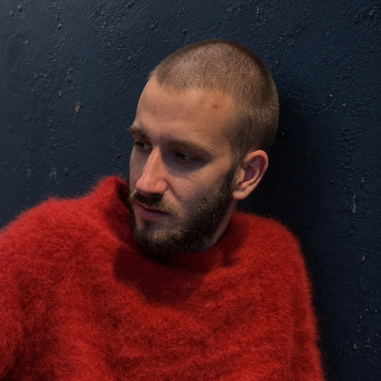 Sergh Pavlov in a red sweater against a dark blue wall